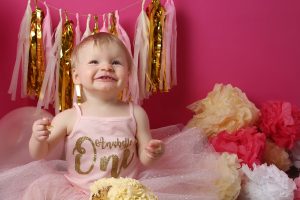 little girl covered in cake for cakesmash photoshoot in west sussex with pink tutu and accessories