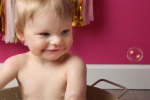 little girl smiling at bubble sitting in bath tub at cakesmash photoshoot in west sussex