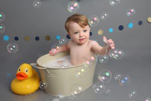 little boy popping bubbles at cakesmash photoshoot in west sussex with grey backdrop and yellow duck