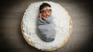 sleeping baby in basket with flower headband and grey wrap on photoshoot in west sussex