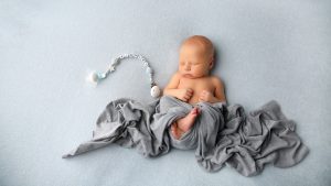 sleeping baby on blue blanket and grey wrap with personalised dummy clip on photoshoot in west sussex