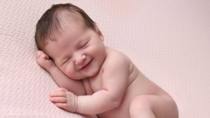 smiling newborn sleeping baby on pink blanket in west sussex