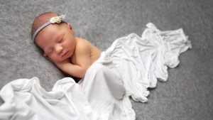 sleeping newborn baby on grey blanket with white wrap and flower headband west sussex photographer