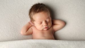 newborn baby on white blanket with hands behind head photoshoot in west sussex