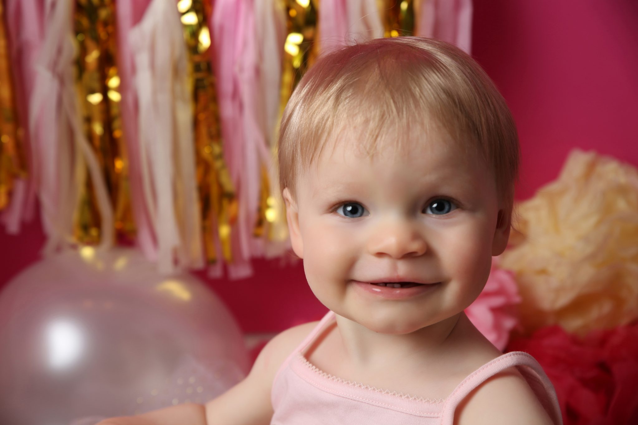 little girl smiling at camera with pink backdrop at photoshoot in west sussex