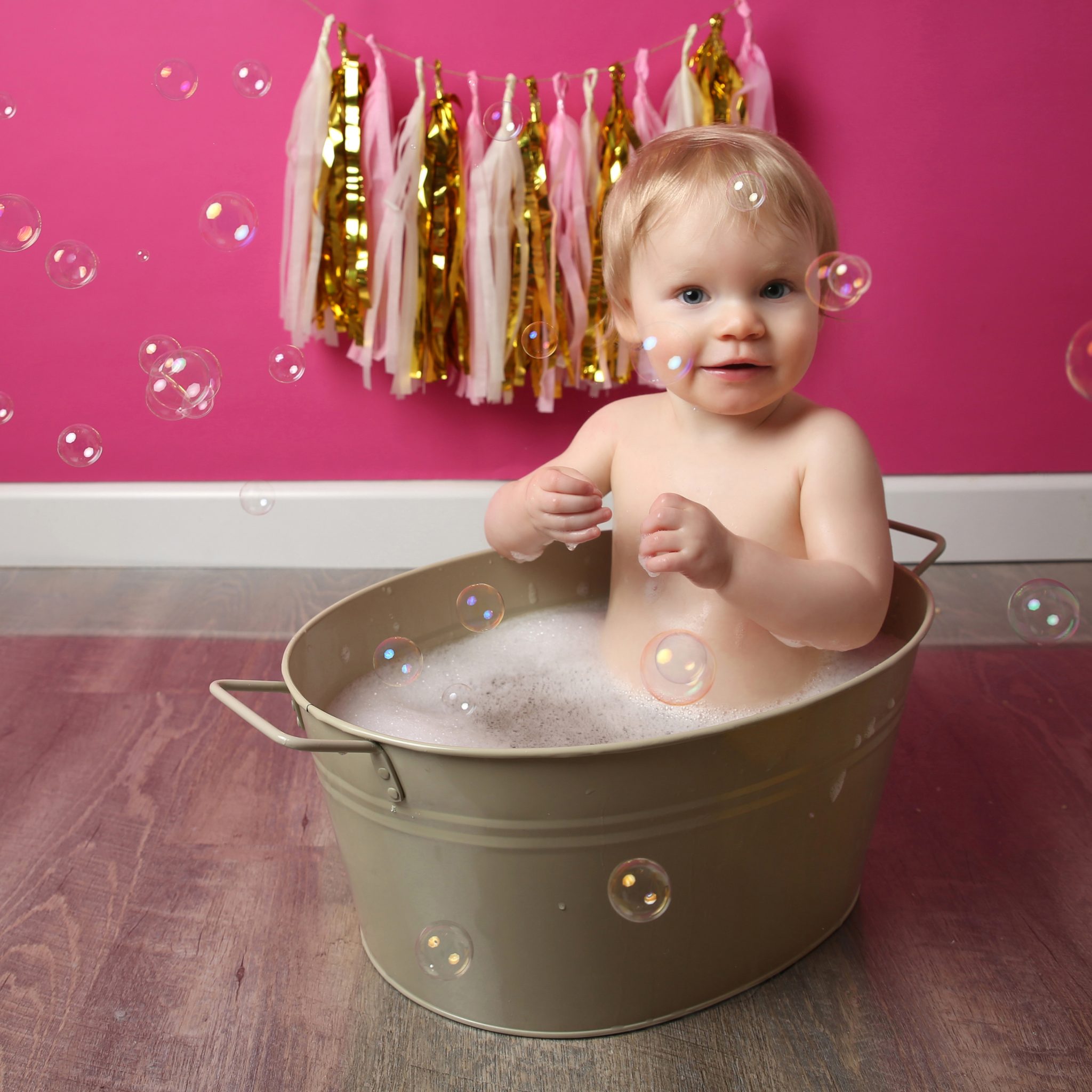 little girl in bathtub with bubbles and pink backdrop at cakesmash photoshoot in east grinstead