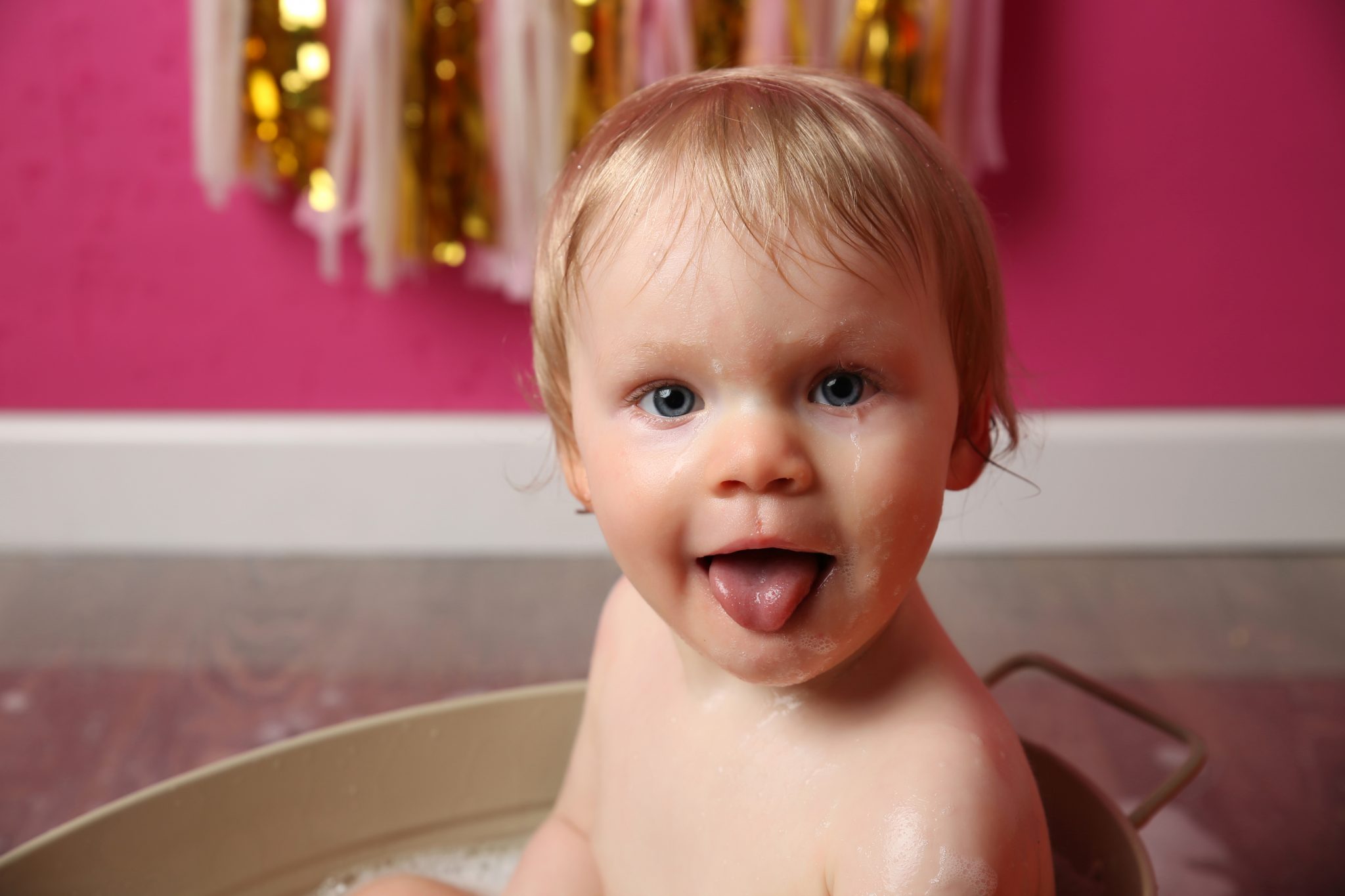 little girl in bath tub being cheeky sticking tongue out at camera at cake smash photoshoot in east grinstead