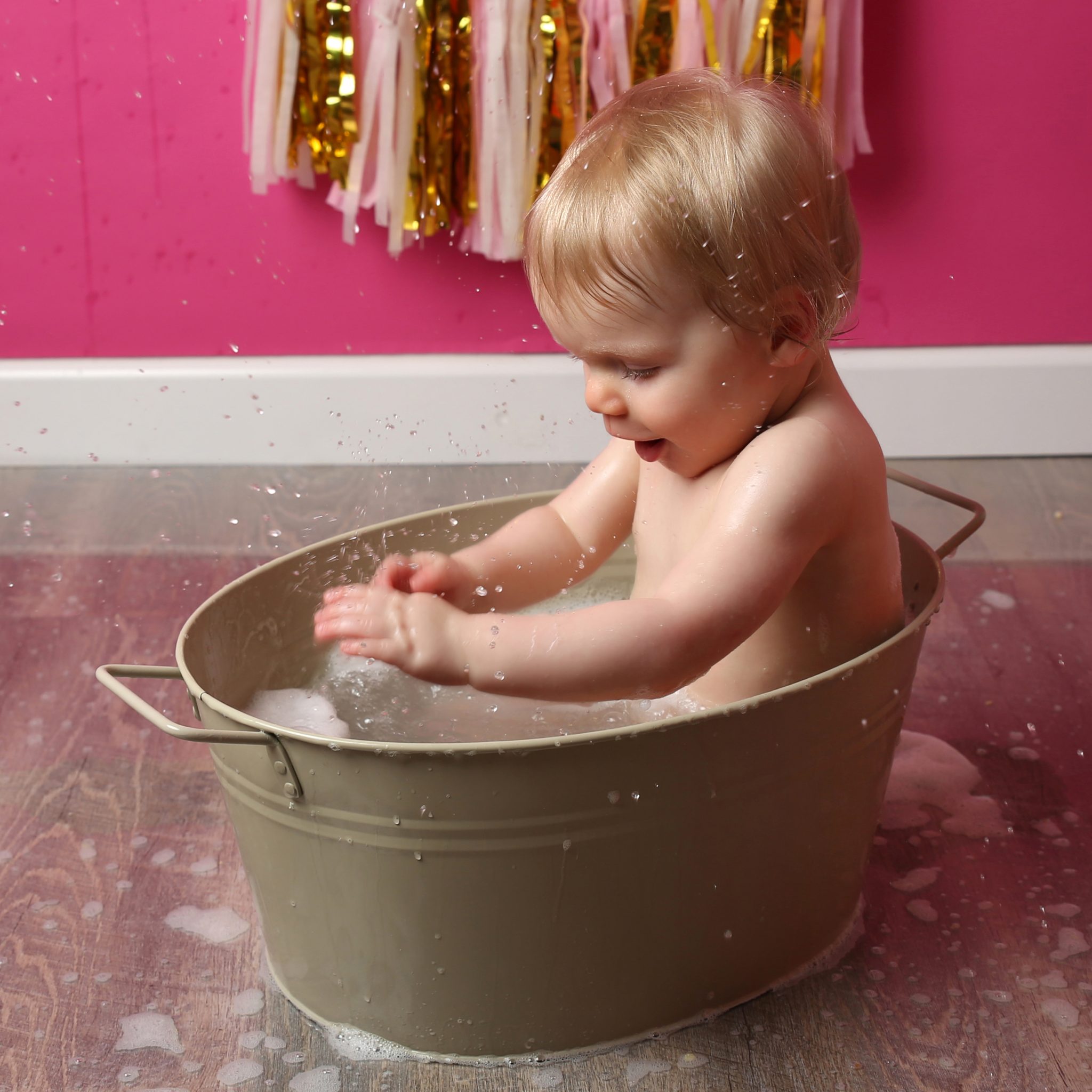 Little girl splashing in bath tub at cakesmash photoshoot in east grinstead with pink backdrop