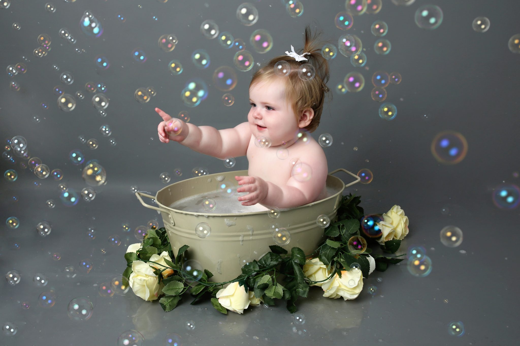 Little girl popping bubbles in bath tub with floral prop at cake smash photoshoot West Sussex