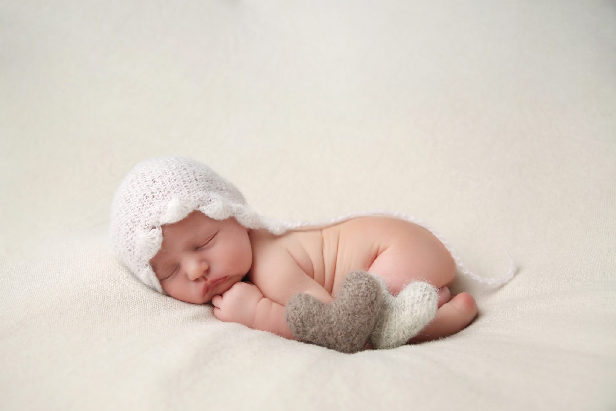 sleeping newborn baby on photoshoot in west sussex on white blanket with natural heart props and white bonnet