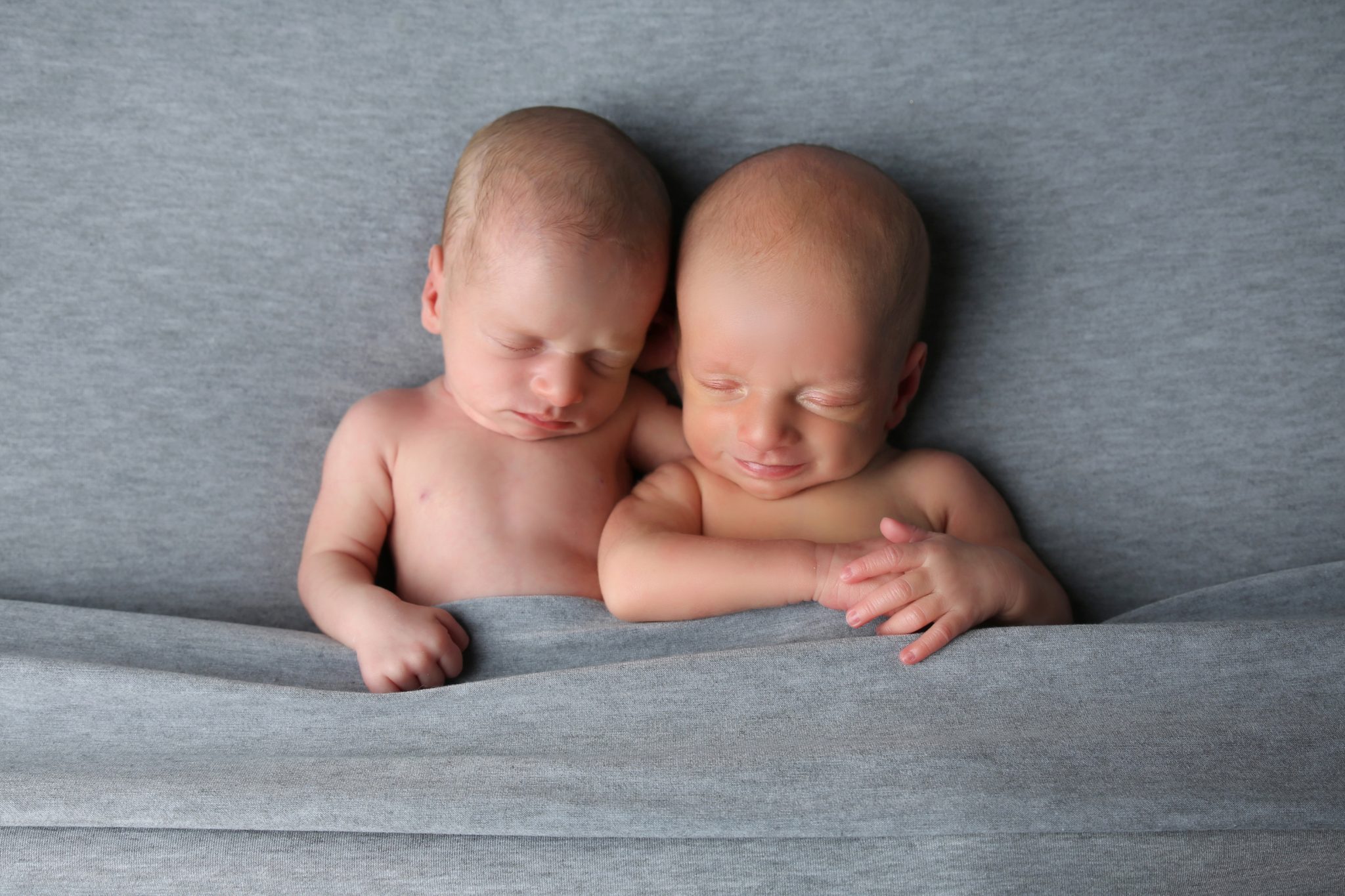 twin babies cuddling and smiling on grey blanket bed on photoshoot in west sussex