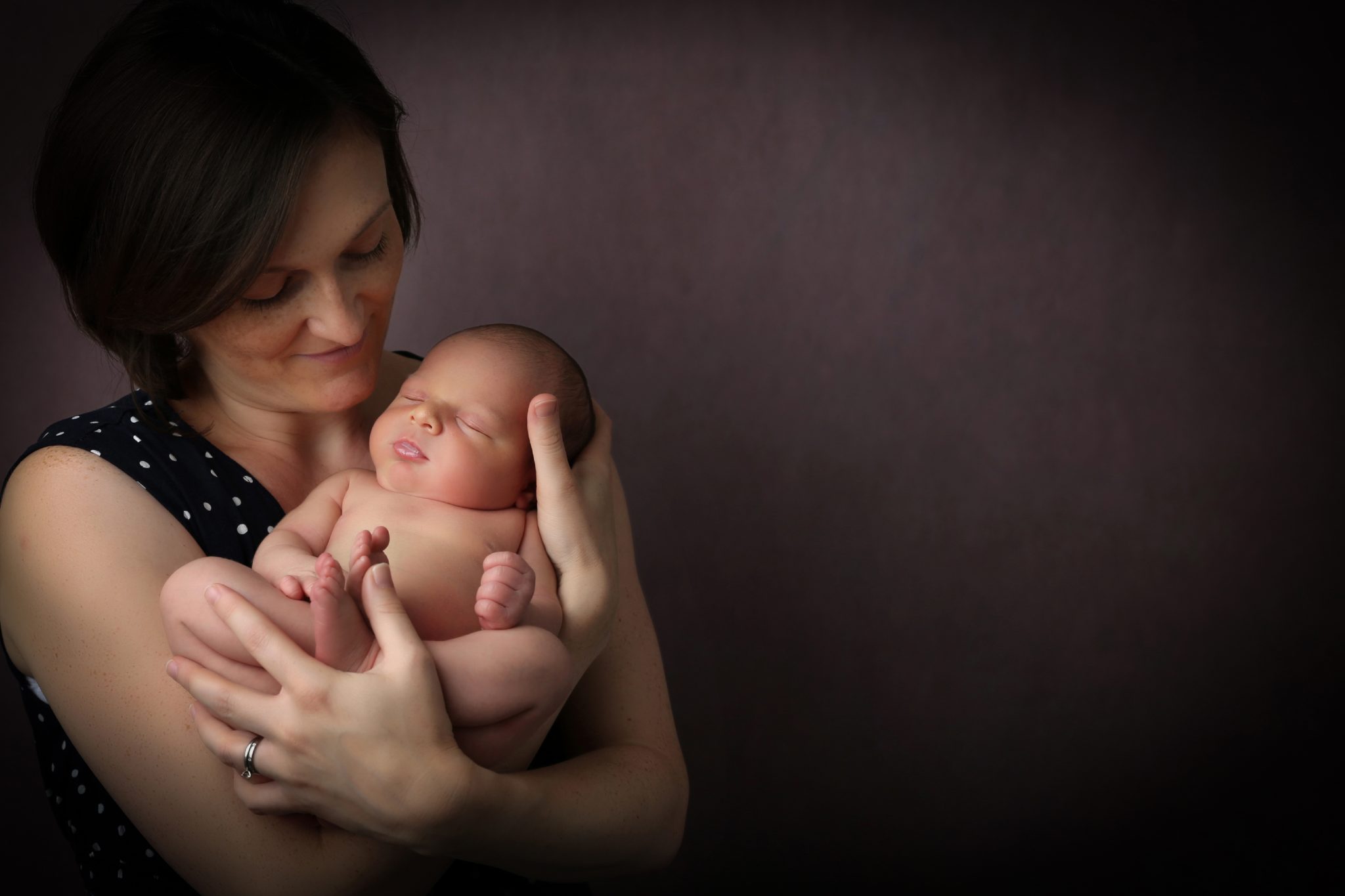 proud mum holding newborn baby sleeping with chestnut backdrop photoshoot in west sussex