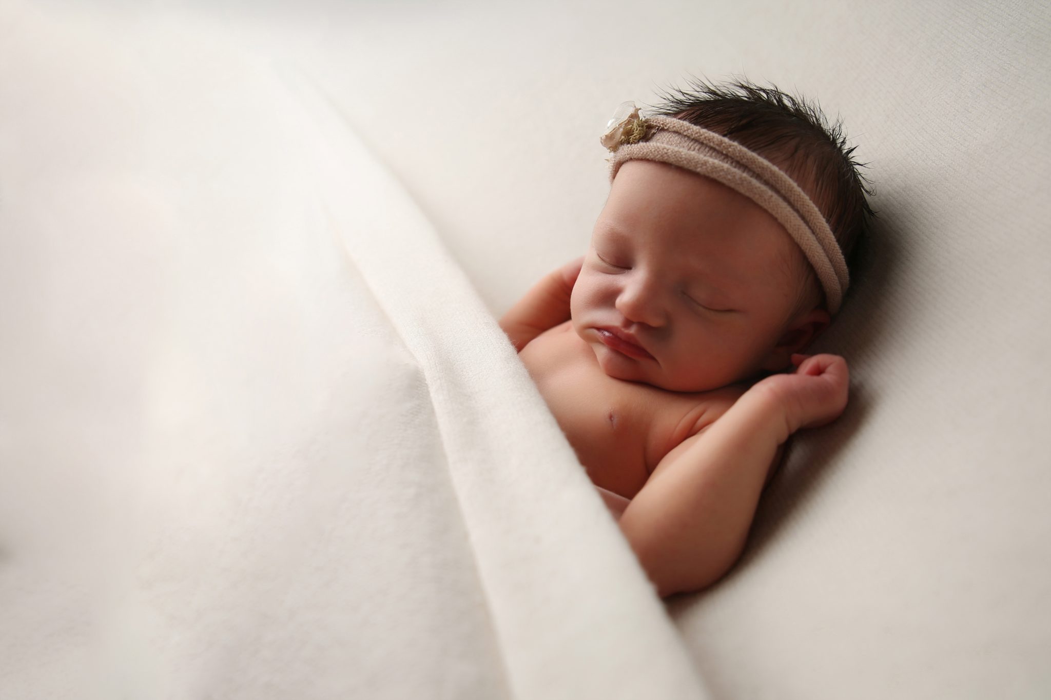 newborn baby asleep in bed white blanket with pink flower headband west sussex photoshoot