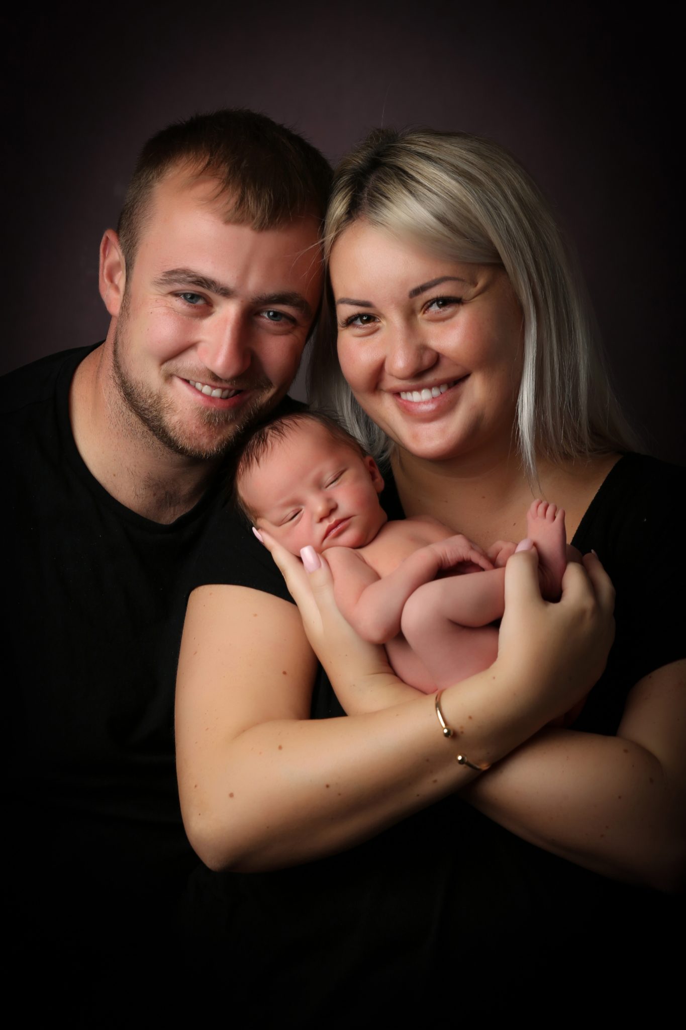 proud parents holding newborn baby on photoshoot in west sussex with chestnut backdrop